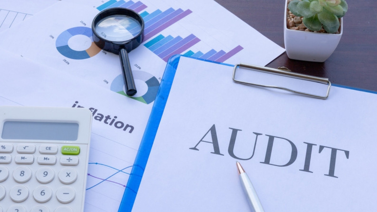 Dossier marqué AUDIT posé sur un bureau, entouré d'une loupe, d'une calculatrice et d'un graphique